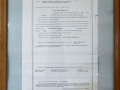 A close-up view of the framed document (Certificate of Incorporation) on the back wall, above and to the left of the glass-front cabinet.