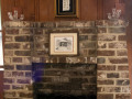 A close-up view of the fireplace in the middle of the left wall of the social hall, showing two candle holders, a framed painting, and the Ten Commandments.