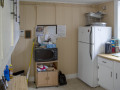 A view of the front wall of the kitchen, showing a microwave oven on a rolling cart. The refrigerator is visible on the left side of the room. The cabinet and the window to the right of the refrigerator are partially visible on the right side of the photograph. The cabinets and counter on the right side of the kitchen are partially visible on the left side of the photograph. The doorway to the kitchen is to the left of the microwave oven.