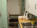 A view of the left side of the back area of the kitchen, showing the outside door to the part of the kitchen. A double sink, a counter, and cabinets are visible on the right side of the photograph.