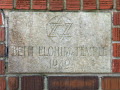 A close-up view of the cornerstone. The cornerstone is visible between the bushes on the left side of the building and the sign on the front lawn.