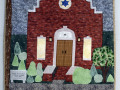 A close-up view of the quilted wall hanging on the far, left side of the front wall of the Social Hall.