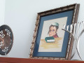 A close-up view of the signed, framed drawing on top of the far, left side of the bookcase. A silver menorah and a bronze bowl are partially visible on either side of the drawing.