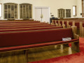 A view of the pews on the right side of the sanctuary, looking from the front of the sanctuary toward the back of the sanctuary. There are nine pews on this side of the sanctuary. The first pew, closest to the bema, has no plaque on it.