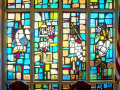 A close-up view of the stained-glass windows between the Beth Israel Synagogue yahrzeit plaque and the American flag at the corner of the bema.
