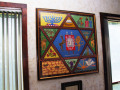 A close-up view of the framed needlepoint tapestry on the back wall of the social hall.