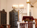 A view of the two yahrzeit plaques to the right of the bema. The yahrzeit plaque on the left side of the photograph is on the end of the right wall of the sanctuary. The yahrzeit plaque to the left of the door is on the front, right wall of the sanctuary. The partially visible door to the right of the yahrzeit plaques leads into the social hall.