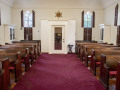A view of the back of the sanctuary, showing the closed, inside door to the entry way. The windows on either side of the door are at the front of the building. There are two glass-front cabinets, one on each side of the entry way, made from packing crates from Lipsitz Department Store on Bay Street.