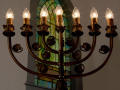 A close-up view of the top of the menorah on the right side of the bema. One of the green stained-glass windows on the front wall of the sanctuary is partially visible behind the menorah.