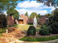 A view of Temple B’nai Israel, looking from the front parking area toward the front of the synagogue. A concrete sculpture of flames sits on a circular grassy area in front of the synagogue. The top of the sanctuary is visible directly above the front doors. The wing to the left of the front doors houses the social hall. The wing to the right of the front doors houses the synagogue offices and a Holocaust display.