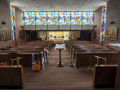 A view of the stained-glass panels at the back of the sanctuary, looking from the front of the sanctuary toward the back of the sanctuary. The social hall and Tree of Life are partially visible below the large stained-glass panels.
