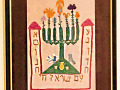 A close-up view of the framed, embroidered menorah on the left wall of the alcove, above the cabinet.