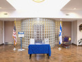 A view of the outer wall of the conference room, looking from the entrance to the synagogue toward the middle of the back wall of the lobby. The brown doors on either side of the flags open into the conference room.