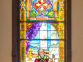 The fifth stained glass window on the left side of the sanctuary. This window is on the back, left wall of the sanctuary, to the left of the front doors.