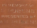 A close-up view of the memoriam tag attached to the Star of David on the Eternal Flame. The tag reads, “In memory of Wolf Rubenstein, presented by (unreadable first name) Rubenstein.”